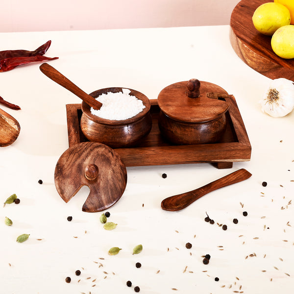 Wooden spice containers with lids on a white surface with spices and herbs.